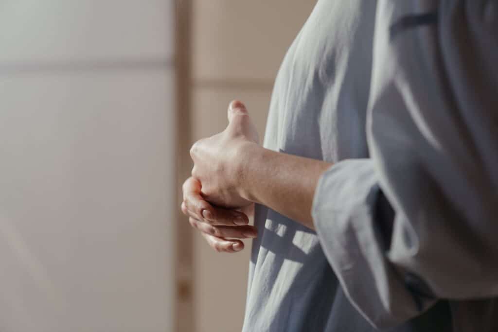 Mujer de perfil con las manos entrelazadas junto a una ventana. Psicóloga perinatal online